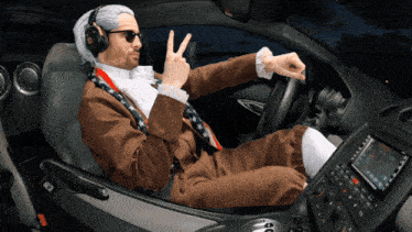 a man in a suit and tie is giving a peace sign while sitting in the driver 's seat of a car