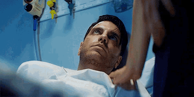 a man is laying in a hospital bed with a nurse standing nearby .