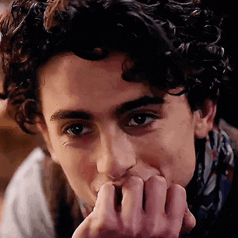 a man with curly hair is biting his nails