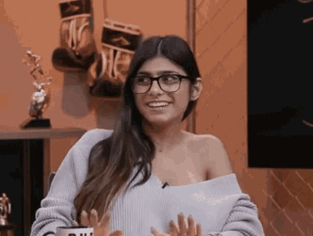 a woman wearing glasses and a sweater is sitting in front of a television .
