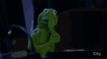kermit the frog is covering his mouth with his hand in a dark room