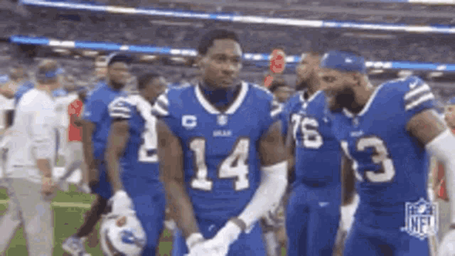 a group of football players in blue uniforms are standing on the field .