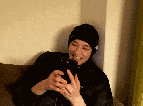 a man wearing a black beanie is laughing while looking at his phone
