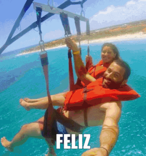 a man and a woman are parasailing in the ocean and the word feliz is above them
