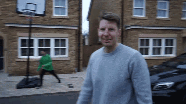 a man in a grey sweater stands in front of a brick house