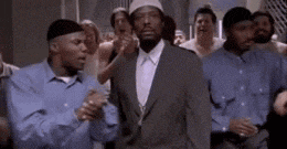 a man in a suit and hat is standing in front of a crowd of people in blue shirts .
