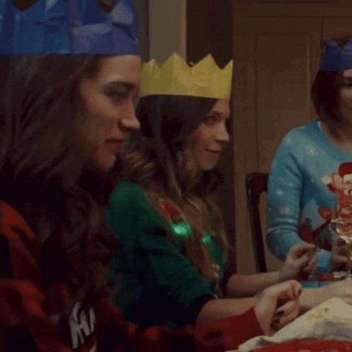 a woman wearing a paper crown sits at a table with two other women