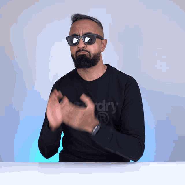 a man wearing sunglasses and a superdry shirt applauds