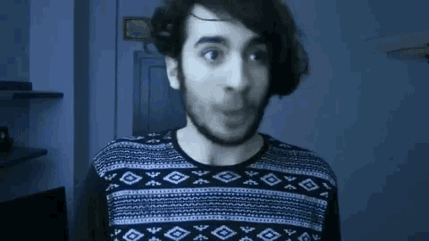 a man with long hair and a beard is wearing a sweater and smiling .