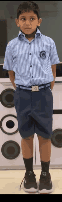 a young boy wearing a striped shirt and shorts is standing in front of speakers .