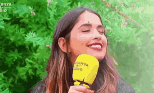 a woman is smiling while holding a yellow microphone in her hand .