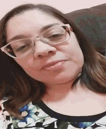 a woman wearing glasses and a floral shirt is making a face