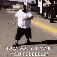 a man is walking down a street with a truck in the background and says `` how does it make you feel ? ''