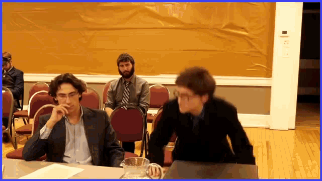 a man in a suit sits at a table with a pitcher of water in front of him