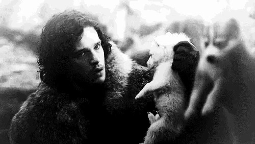 a black and white photo of a man in a fur coat standing next to a wolf .