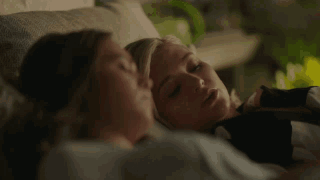 two women are laying on a couch and looking at each other