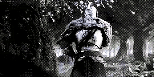 a man in armor is walking through a dark forest .