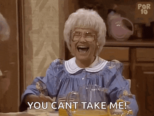 an elderly woman is sitting at a table laughing and saying `` you can t take me ! ''