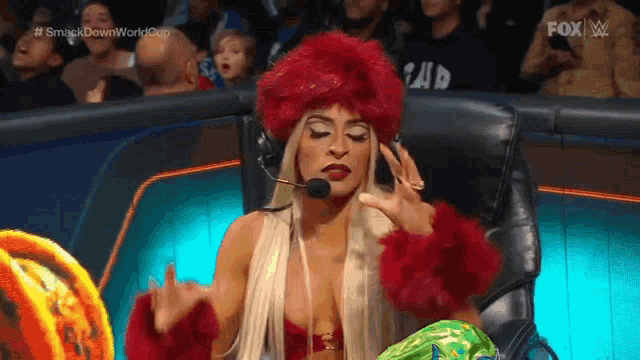 a woman in a red wig is sitting in a chair with a microphone in her hand .