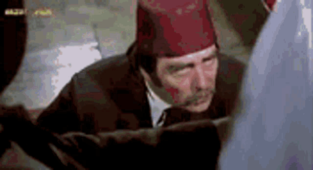 a man in a suit and tie is wearing a red hat and looking at something .