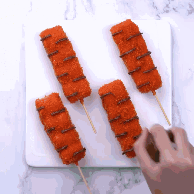 a white plate with four fried food sticks with chocolate sauce on them