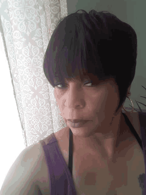 a woman wearing a purple tank top and black bra looks at the camera