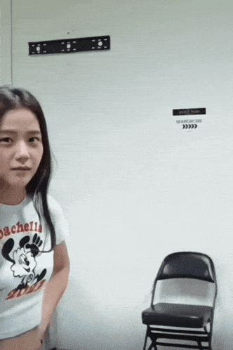 a woman wearing a mickey mouse shirt is standing in front of a chair