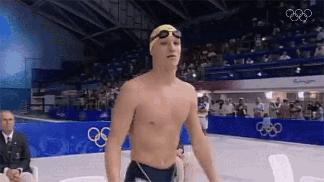 a shirtless swimmer wearing a yellow swim cap and goggles is standing in front of a crowd .