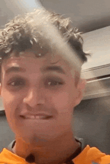 a young man with curly hair is smiling and looking at the camera while wearing an orange shirt .