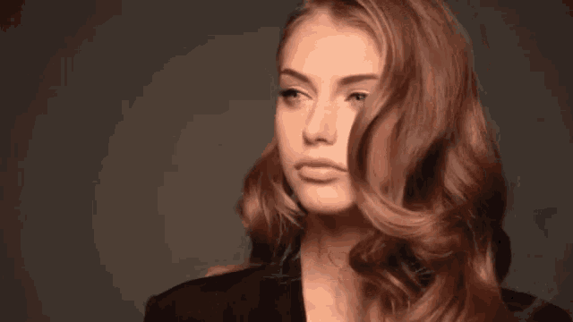 the woman is wearing a black jacket and holding her hair