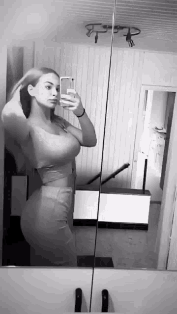 a black and white photo of a woman taking a selfie in a mirror .