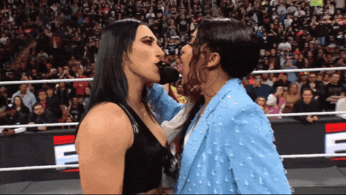 two women kissing in a wrestling ring with the letter e in the background