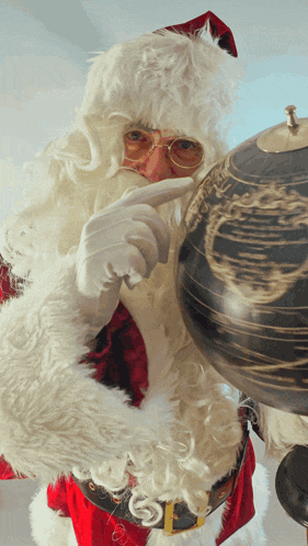 a santa claus pointing at a globe with a map of the earth on it