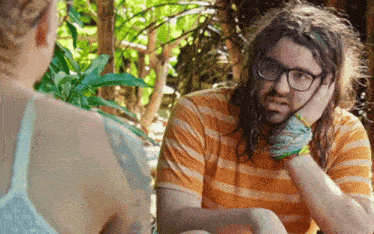 a man with long hair and glasses is sitting next to a woman with a tattoo on her arm .
