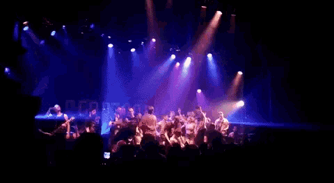 a group of people are dancing on a stage with purple lights behind them