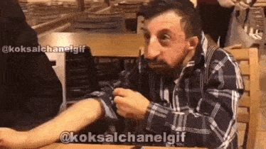 a man in a plaid shirt is sitting at a table in a restaurant and holding his arm .