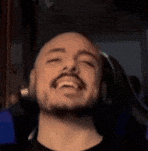 a bald man with a beard is wearing headphones and laughing with his eyes closed .