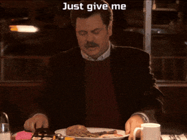 a man is sitting at a table with a plate of food and a caption that says just give me all the bacon and eggs