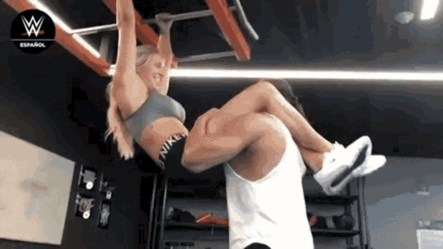 a man is carrying a woman in his arms in a gym with a w logo in the background