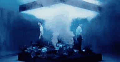 a group of people are standing in a dark room with smoke coming out of a box .