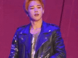 a man in a blue leather jacket is singing into a microphone on stage .