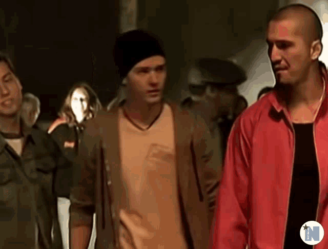 a man in a red jacket stands next to another man in a black hat