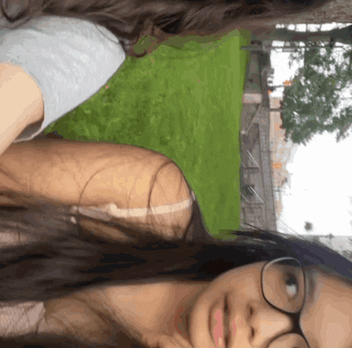 a girl wearing glasses is sitting next to another girl in a park