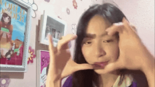 a girl is making a heart shape with her hands in front of a framed picture
