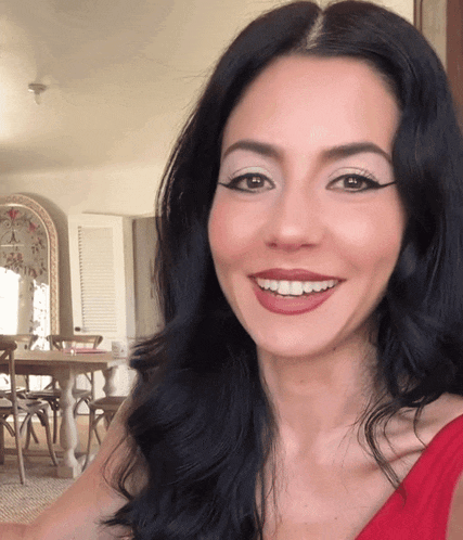 a woman with long black hair is smiling in front of a table and chairs