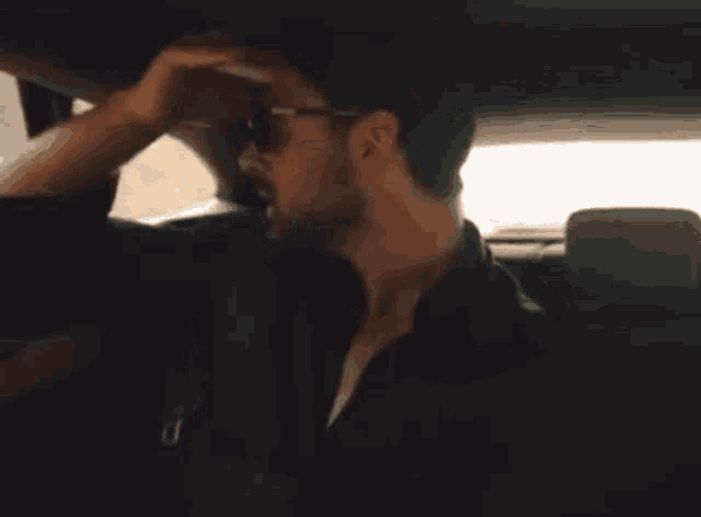 a man with a beard is sitting in the back seat of a car talking to someone .