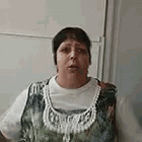 a woman in a white shirt and a green vest is standing in front of a refrigerator .