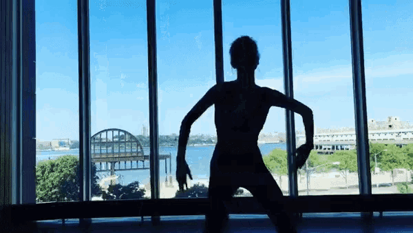a silhouette of a woman dancing in front of a window overlooking a body of water