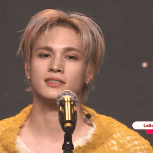 a man in a yellow sweater is singing into a microphone with the word lese in the corner