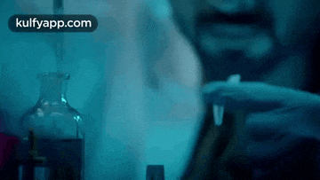 a man is smoking a cigarette in front of a bottle of liquid with the words kulfyapp.com on the bottom right